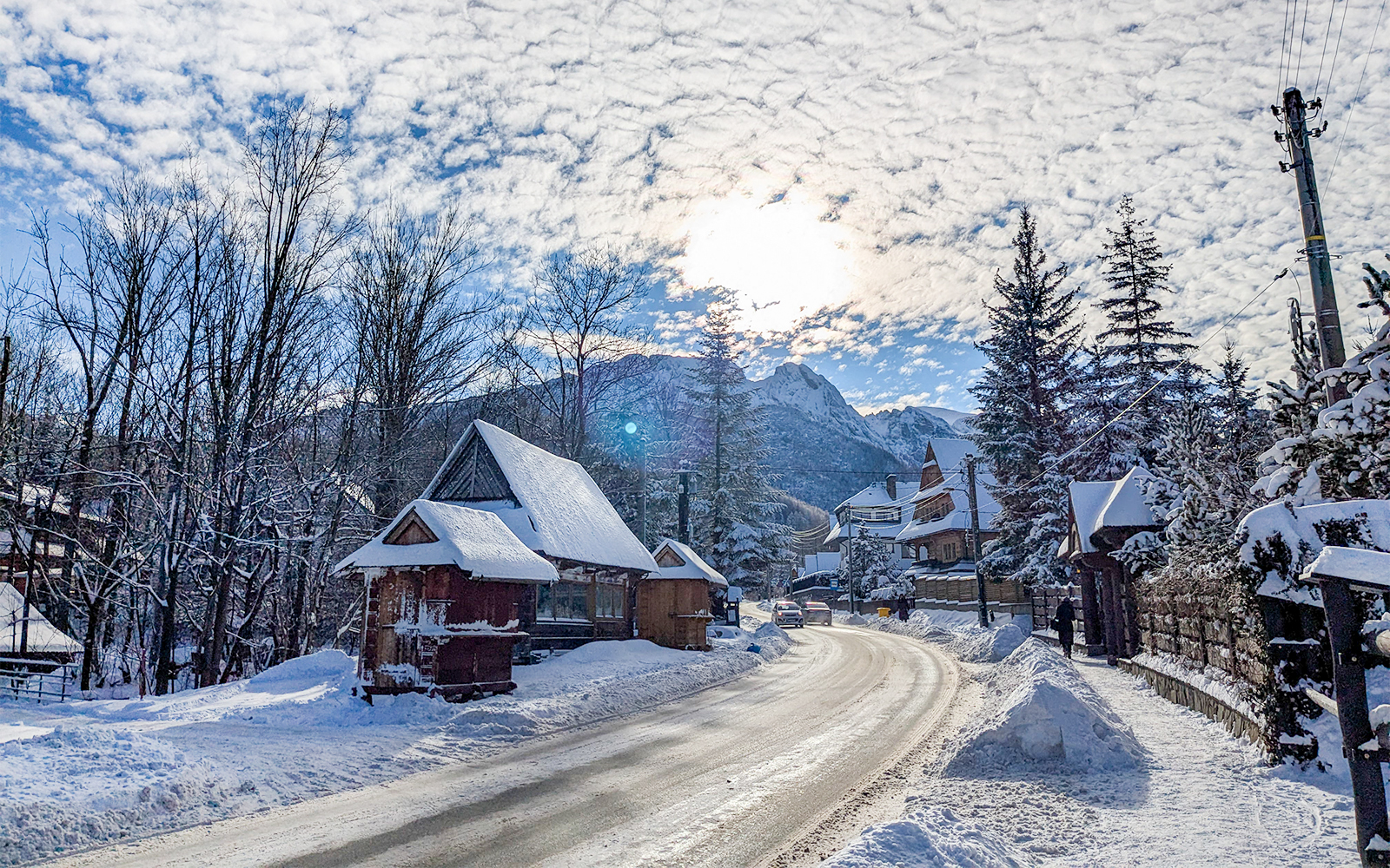 Wooden houses covered in snow along a road in Zakopane, with mountains in the background.