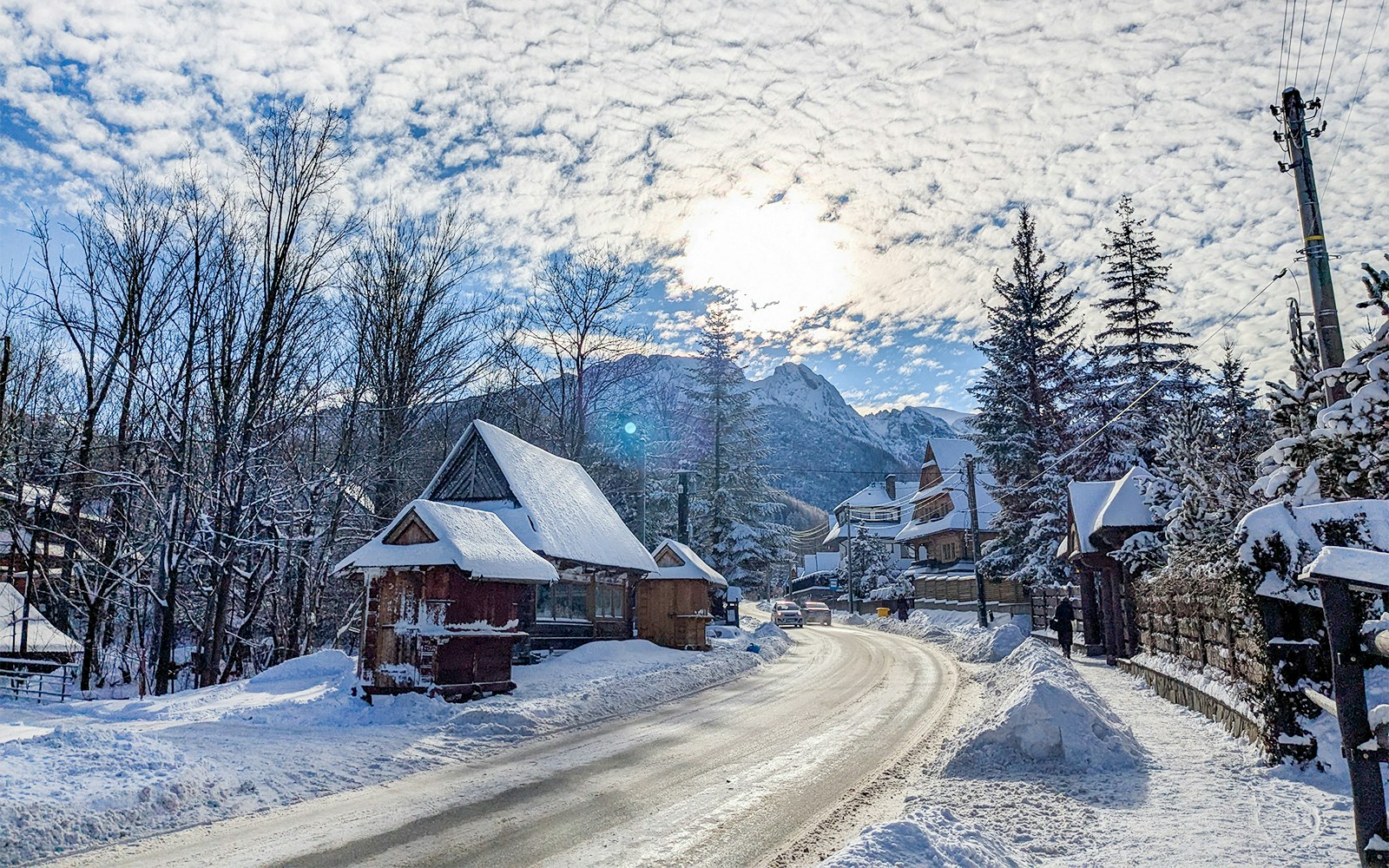 Wooden houses covered in snow along a road in Zakopane, with mountains in the background.