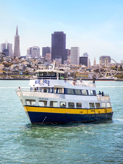 Blue and Gold Fleet ferry cruising in San Francisco Bay with city skyline in the background.