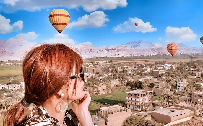 Hot air balloons over Luxor landscape with a person viewing the scene.