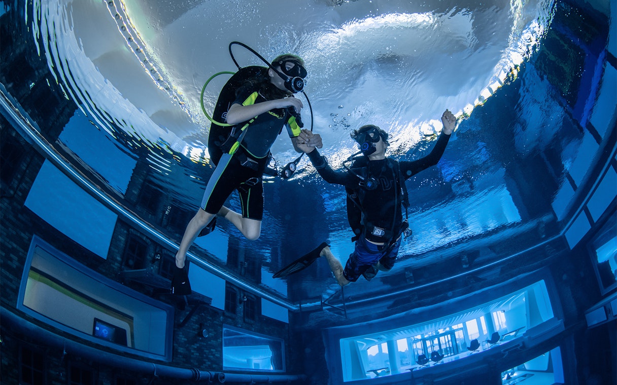 Scuba divers exploring Deep Dive Dubai's underwater city.