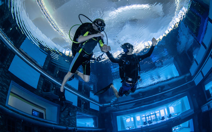 Scuba divers exploring Deep Dive Dubai's underwater city.