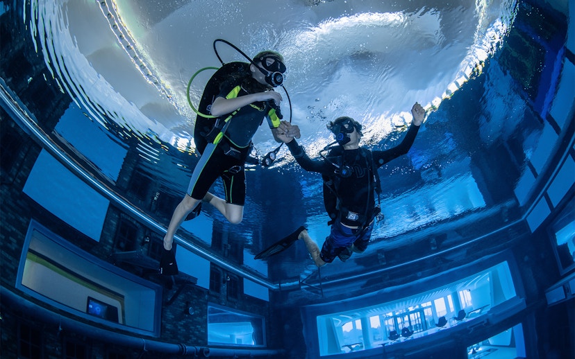 Scuba divers exploring Deep Dive Dubai's underwater city.
