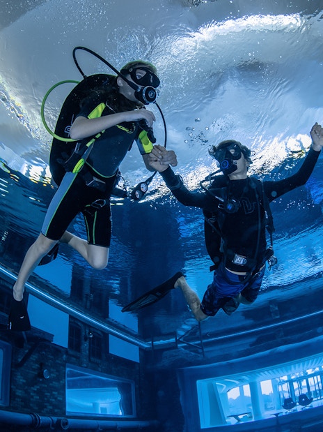 Scuba divers exploring Deep Dive Dubai's underwater city.