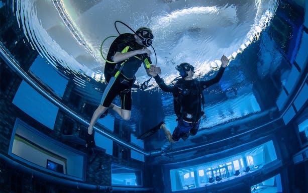 Scuba divers exploring Deep Dive Dubai's underwater city.