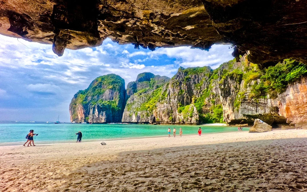 Beach view with tourists at Maya Bay, Phi Phi Islands, Krabi, surrounded by limestone cliffs.