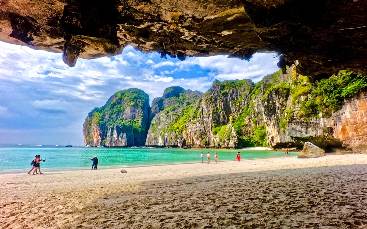 Beach view with tourists at Maya Bay, Phi Phi Islands, Krabi, surrounded by limestone cliffs.