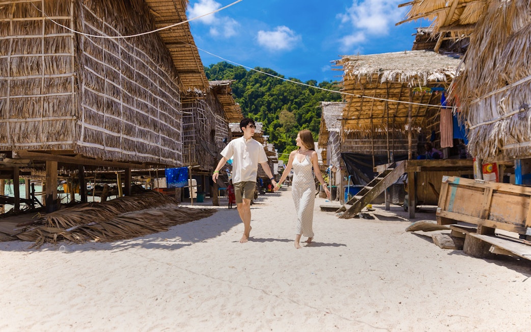 Tourists walking in Moken village with traditional stilt houses and lush greenery.