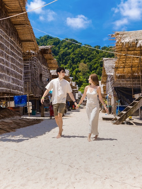 Tourists walking in Moken village with traditional stilt houses and lush greenery.