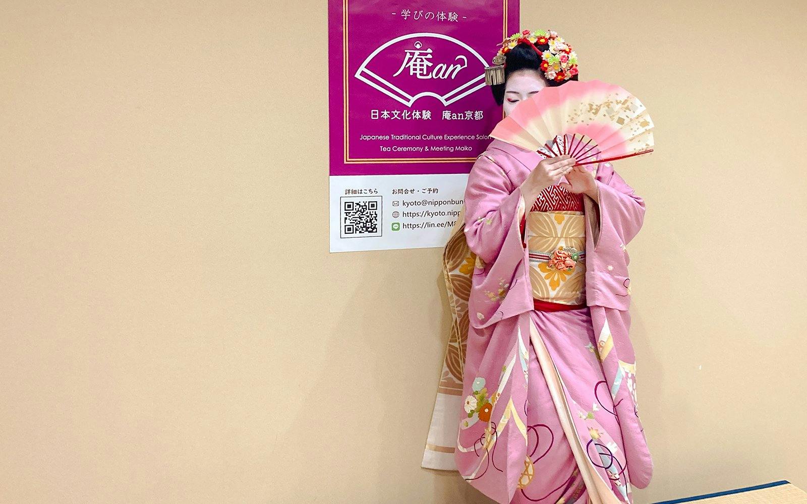 Maiko in pink kimono holding a traditional Japanese fan at a tea ceremony in Kyoto.