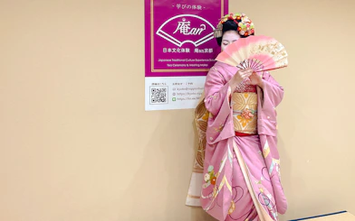 Maiko in pink kimono holding a traditional Japanese fan at a tea ceremony in Kyoto.