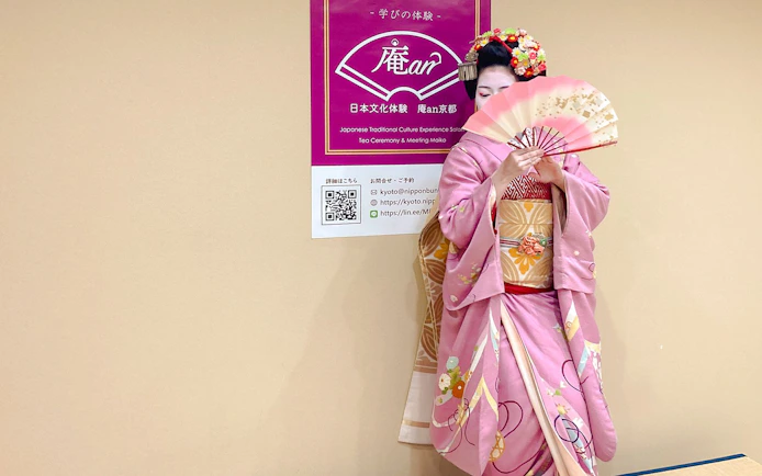 Maiko in pink kimono holding a traditional Japanese fan at a tea ceremony in Kyoto.