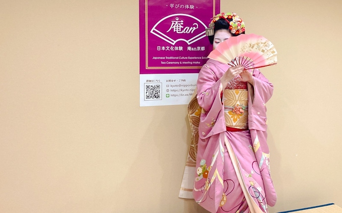 Maiko in pink kimono holding a traditional Japanese fan at a tea ceremony in Kyoto.