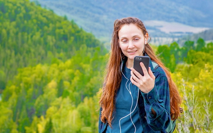 Woman using audio guide on smartphone in a lush green forest setting.