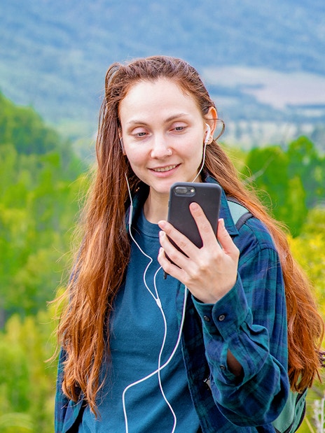 Woman using audio guide on smartphone in a lush green forest setting.