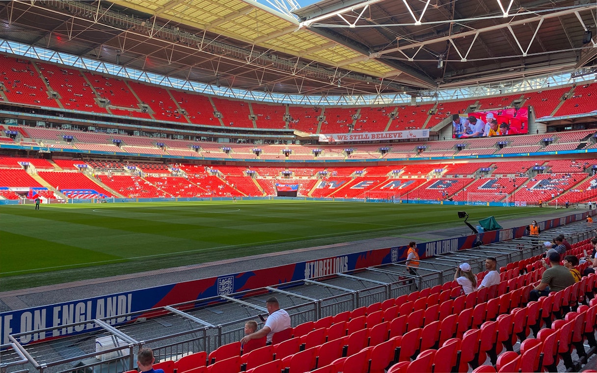 Wembley Stadium interior with red seats and green pitch, part of guided tour experience.