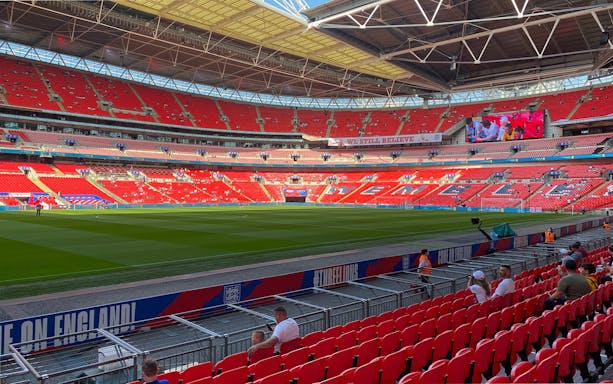 Wembley Stadium interior with red seats and green pitch, part of guided tour experience.
