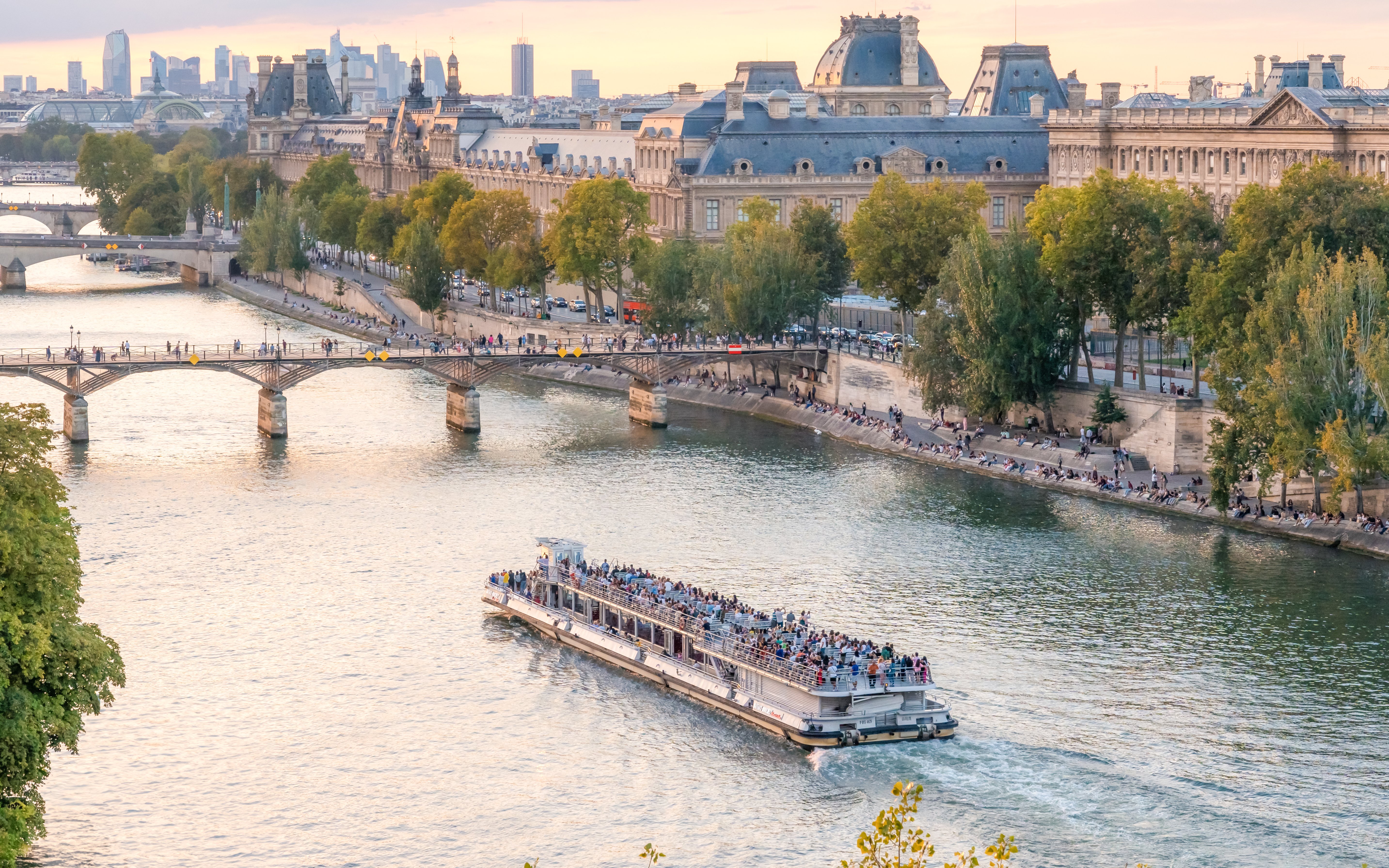 Seine River cruise boat passing by Paris landmarks during evening.