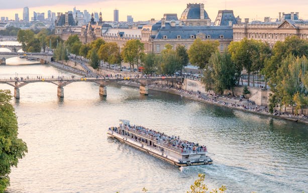 Seine River cruise boat passing by Paris landmarks during evening.