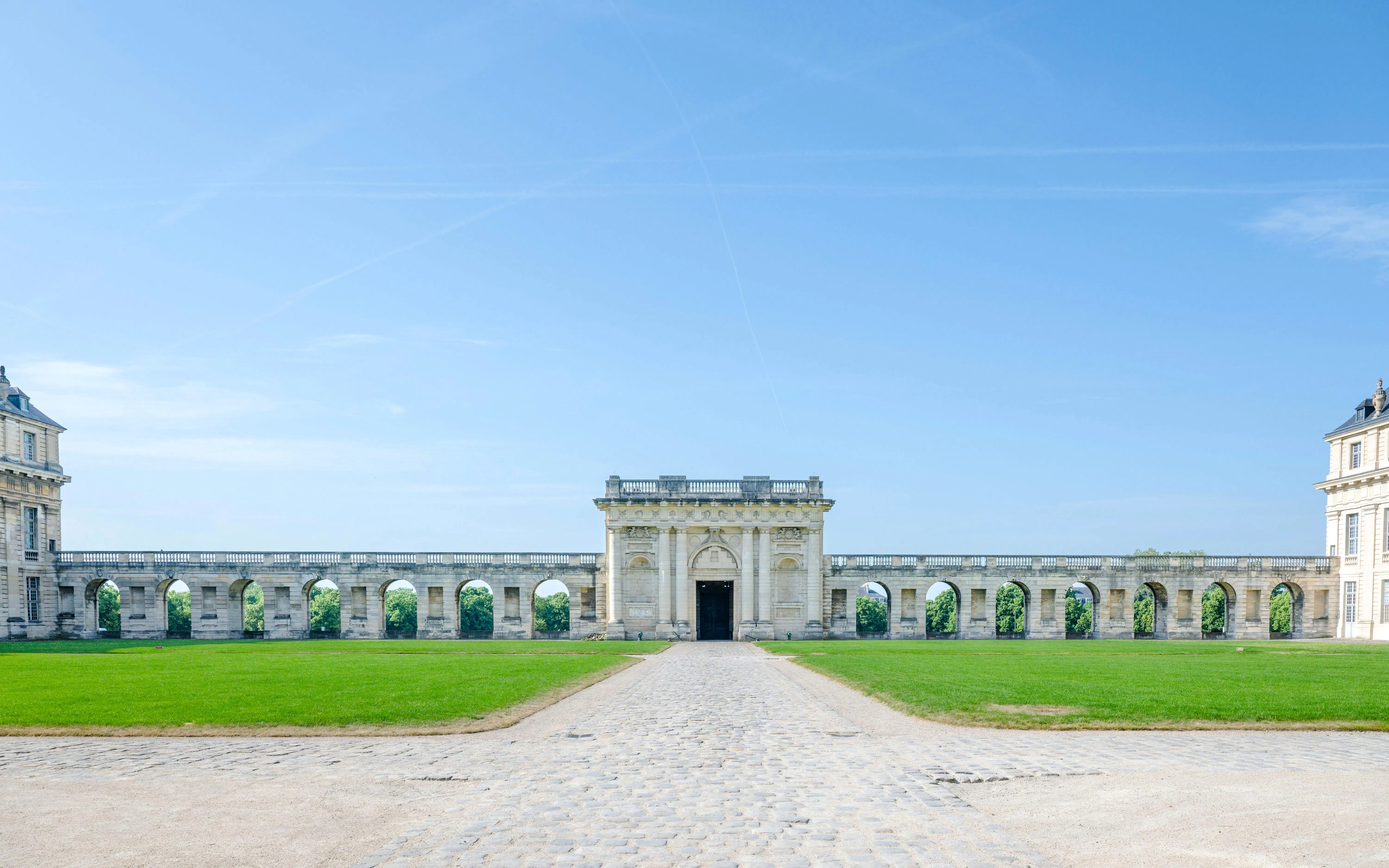 Château de Vincennes facade with stone arches and green lawn in Paris, France.