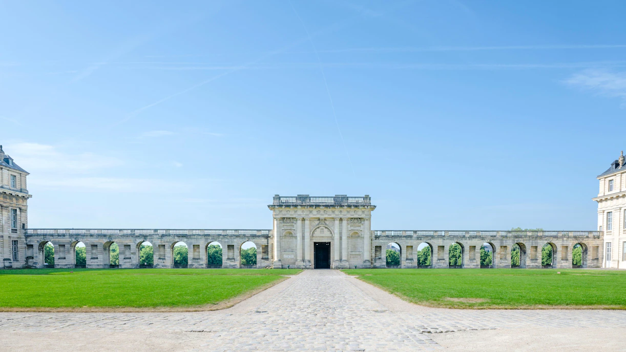 Château de Vincennes facade with stone arches and green lawn in Paris, France.