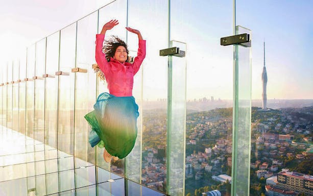 Person jumping on glass platform at Istanbul Emaar SkyView with cityscape in background.
