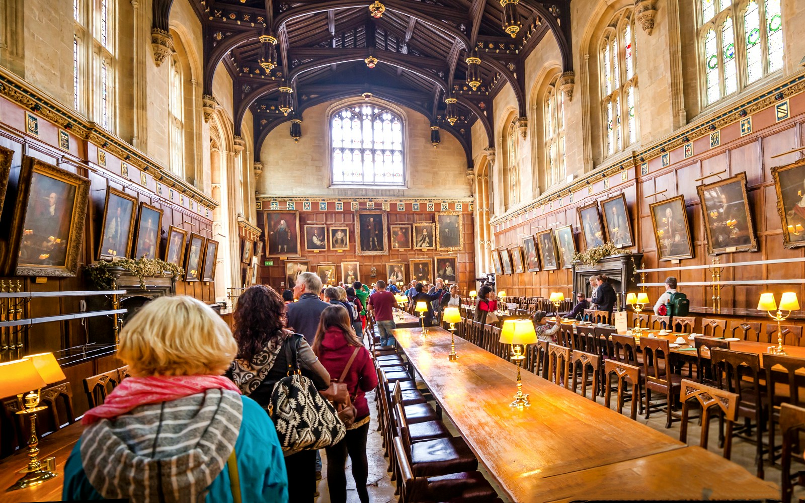 Dining hall at Oxford University with visitors exploring historic portraits.