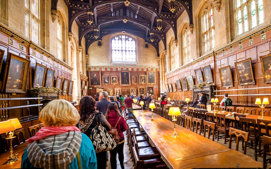 Dining hall at Oxford University with visitors exploring historic portraits.