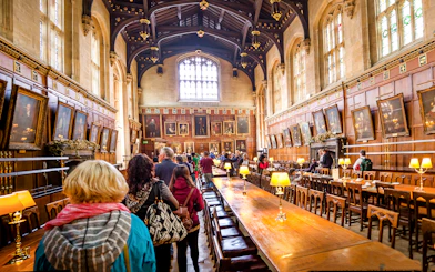Dining hall at Oxford University with visitors exploring historic portraits.