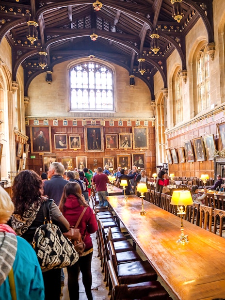 Dining hall at Oxford University with visitors exploring historic portraits.