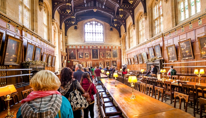Dining hall at Oxford University with visitors exploring historic portraits.