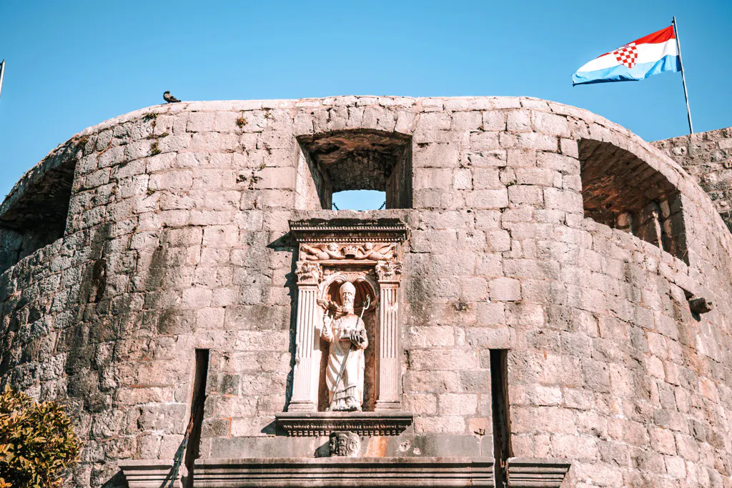 Stone fortress wall with a statue and Croatian flag, Dubrovnik.