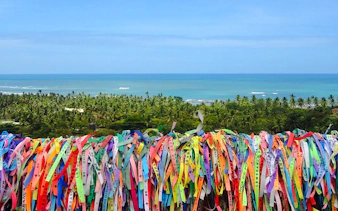 Colorful ribbons tied on a fence overlooking palm trees and ocean in Arraial d'Ajuda, Porto Seguro.