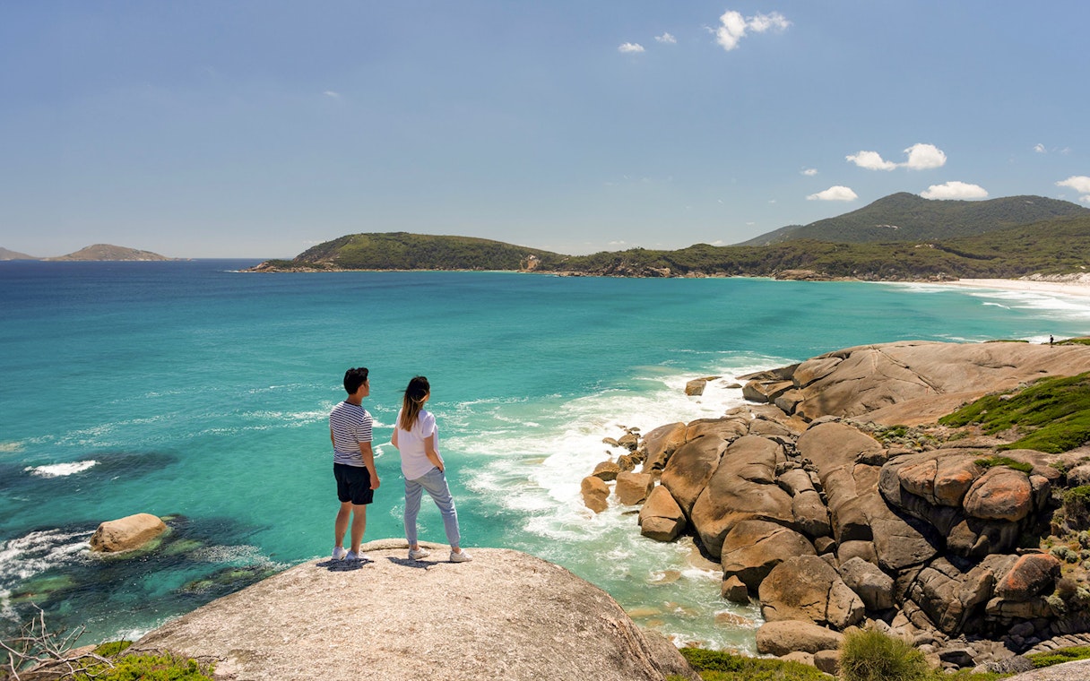 Couple overlooking turquoise waters and rocky coastline at Wilsons Promontory National Park, Australia.