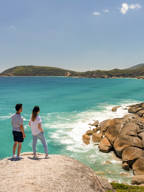 Couple overlooking turquoise waters and rocky coastline at Wilsons Promontory National Park, Australia.