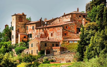 Historic stone buildings in Val D’Orcia, Tuscany, surrounded by lush greenery.