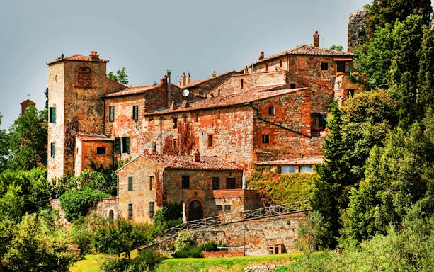 Historic stone buildings in Val D’Orcia, Tuscany, surrounded by lush greenery.