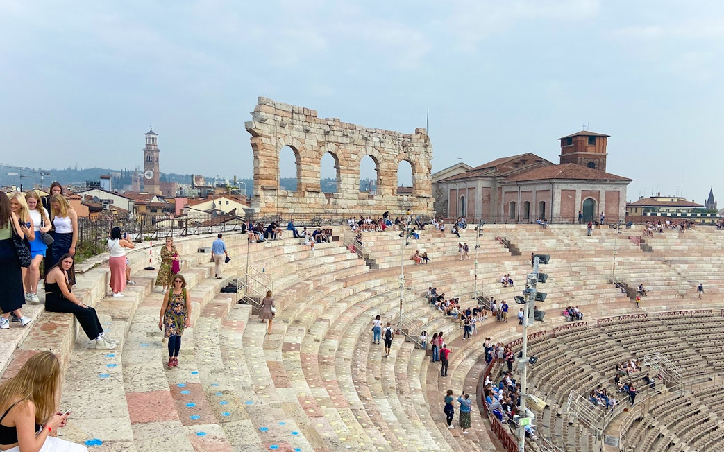 Verona Arena arches with visitors seated on ancient stone steps.