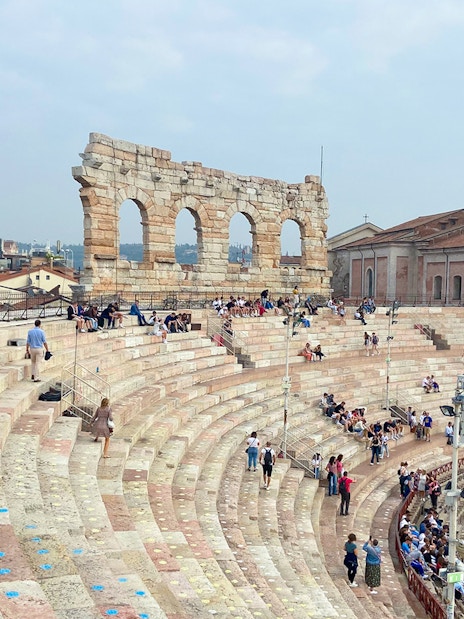 Verona Arena arches with visitors seated on ancient stone steps.