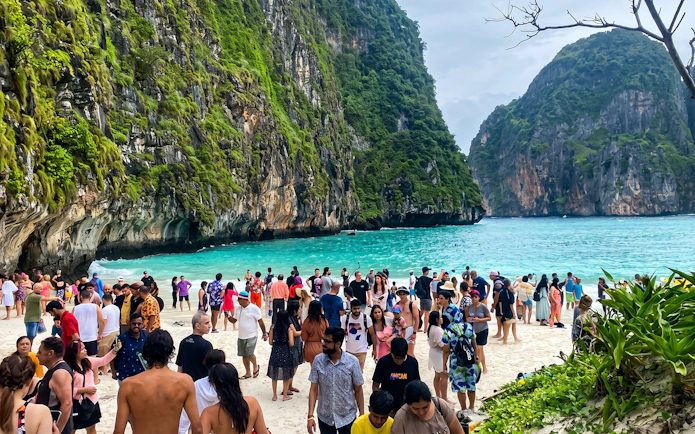 Crowd enjoying the beach at Maya Bay, Phi Phi Islands, with limestone cliffs and turquoise water.