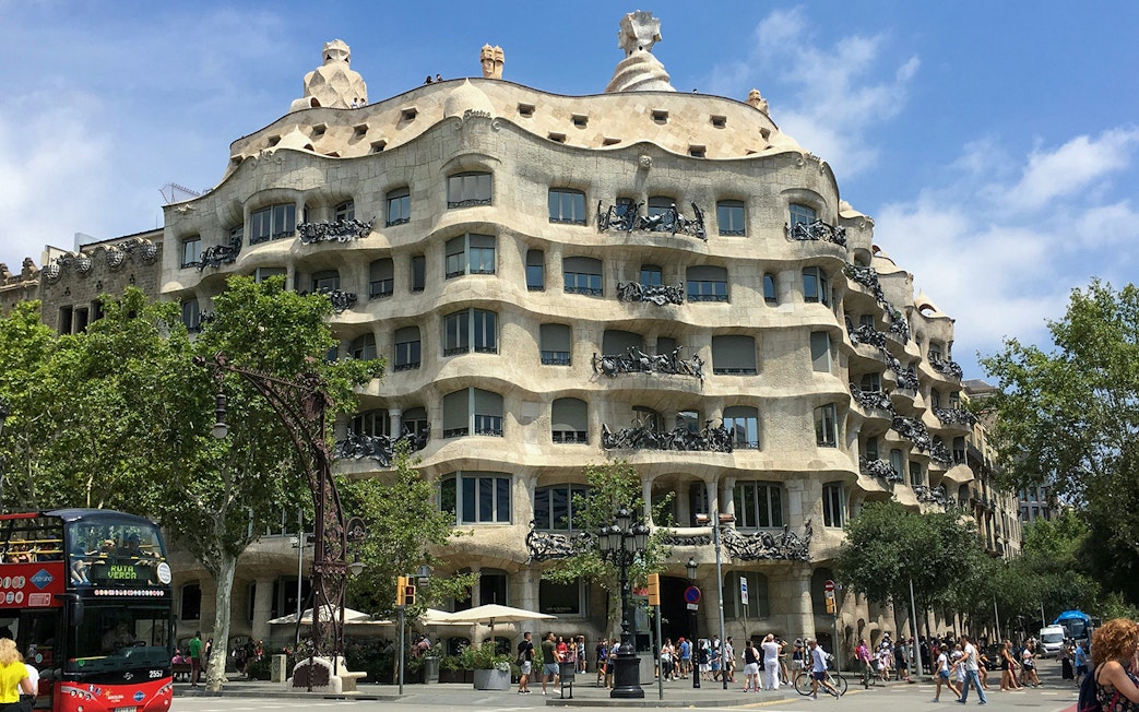 Casa Mila viewed from across the street, Barcelona, with tourists and a tour bus.