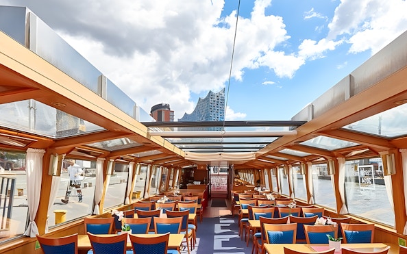 Interior of a tour boat with seating, Elbphilharmonie visible through windows, Hamburg Harbor Cruise.