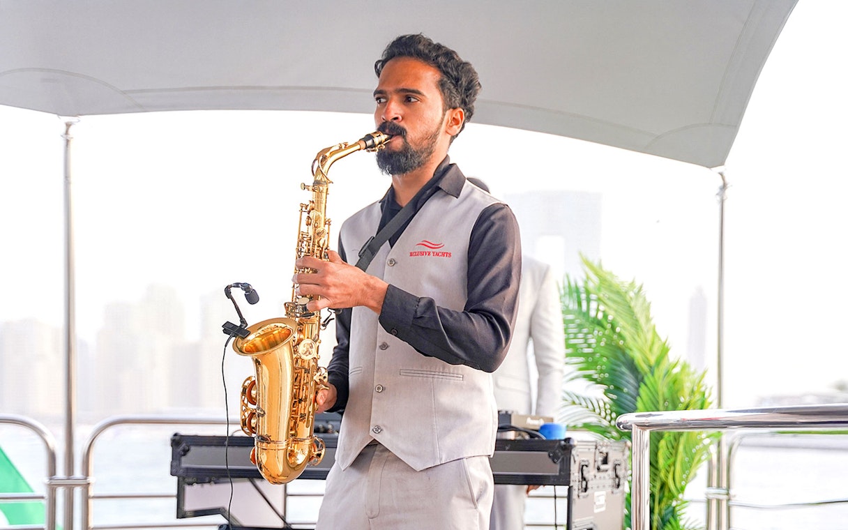 Saxophonist performing on Sunseeker superyacht with city skyline in background.