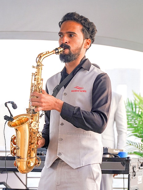 Saxophonist performing on Sunseeker superyacht with city skyline in background.