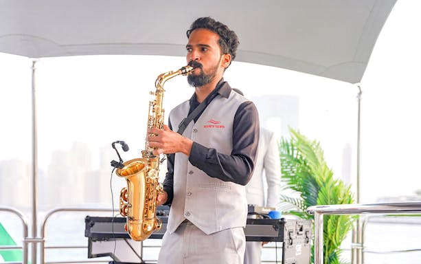 Saxophonist performing on Sunseeker superyacht with city skyline in background.