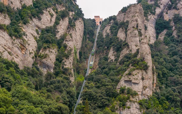 Train ascending Montserrat mountain near the monastery, surrounded by rocky cliffs and greenery.