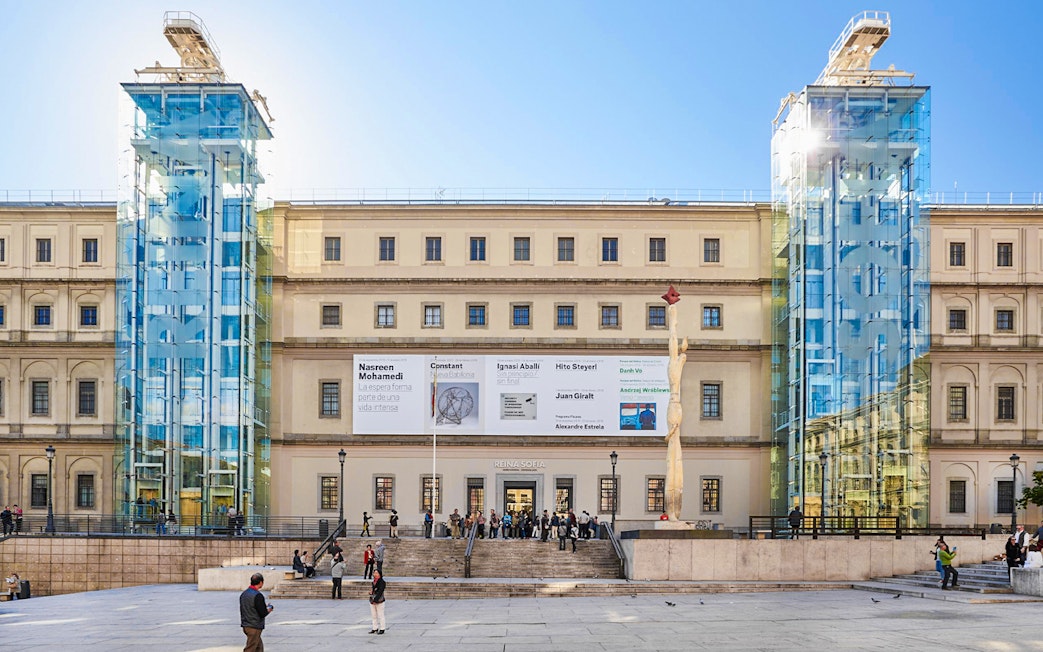 Reina Sofia Museum entrance with glass elevators and visitors in Madrid.