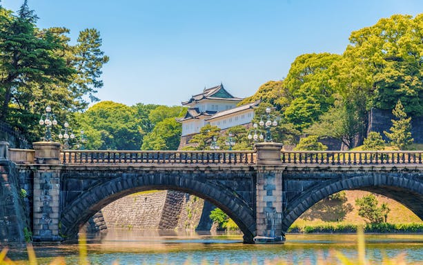 Tokyo Imperial Palace with Nijubashi Bridge in foreground, surrounded by lush greenery.