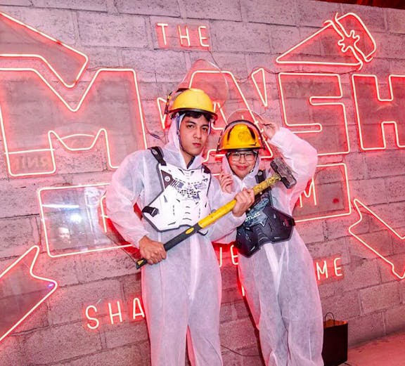 Visitors in protective gear holding sledgehammers at a Smash Room experience.