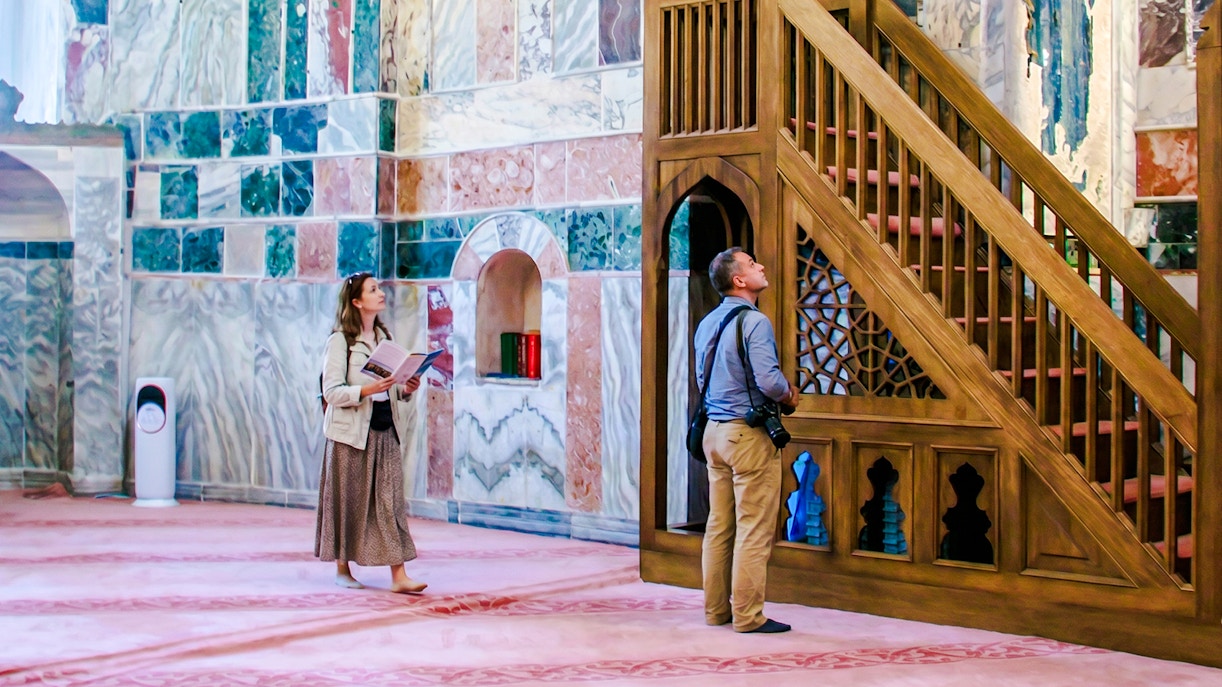 Guests exploring the interior of Kariye Mosque, Istanbul, near ornate wooden staircase.